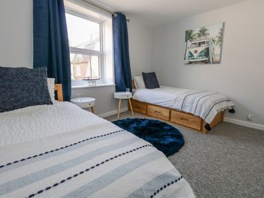 A bedroom with two single beds blue pillows round blue rug and a window with blue curtains at Cove Street Cottage in Weymouth