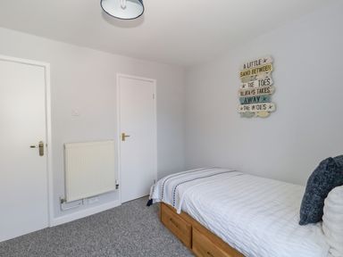 A bedroom with a single bed two white doors a wall radiator and a decorative sign on the wall at Cove Street Cottage in Weymouth