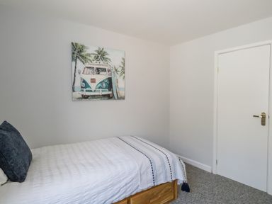 A bedroom with a single bed a white door and a wall painting of a van at Cove Street Cottage in Weymouth
