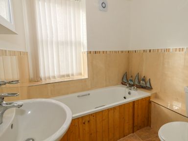 A bathroom with a bathtub wooden paneling a sink and a window with vertical blinds at Cove Street Cottage in Weymouth