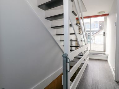 A staircase with white railings and black steps next to a glass sliding door leading outside at Cove Street Cottage in Weymouth
