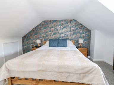A bedroom with a wooden bed a patterned wallpaper behind the bed and two bedside tables with lamps at Cove Street Cottage in Weymouth