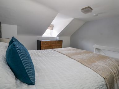 A bedroom with a bed with blue pillows beside a window and a chest of drawers at Cove Street Cottage in Weymouth