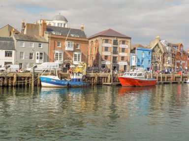 A harbor with boats docked and buildings along the waterfront at Cove Street Cottage in Weymouth