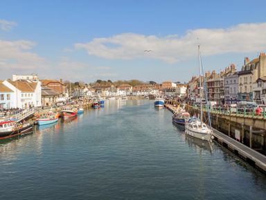 A harbor with boats docked along the water and buildings lining both sides at Cove Street Cottage in Weymouth