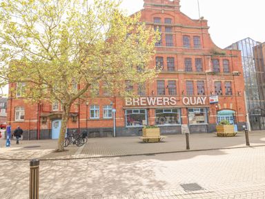 An exterior view of a red brick building with the sign Brewers Quay and a tree in front in Weymouth