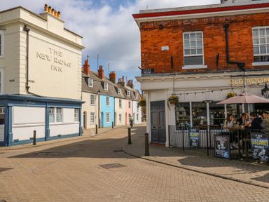 A street corner with a pub and colorful houses along a cobbled road at Cove Street Cottage in Weymouth