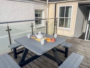 An outdoor patio with a gray picnic table set and a teapot with cups on the table at Cove Street Cottage in Weymouth