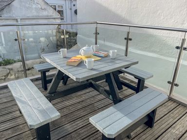 An outdoor patio with a picnic table set including a teapot mugs and books at Cove Street Cottage in Weymouth