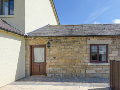 An exterior view of a stone and plaster building with a wooden door and window at Dairymaid's Cottage in Amble