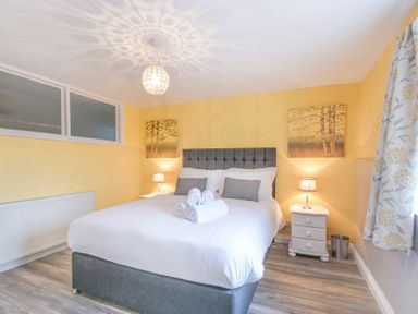 A bedroom with a gray bed a white bedside table lamps and floral curtains at Dairymaid's Cottage in Amble
