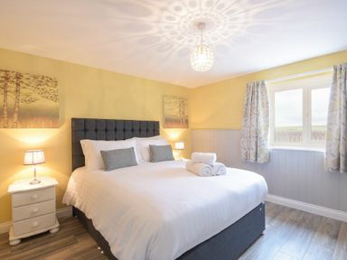 A bedroom with a large bed bedside tables with lamps wall art and a window with curtains at Dairymaid's Cottage in Amble