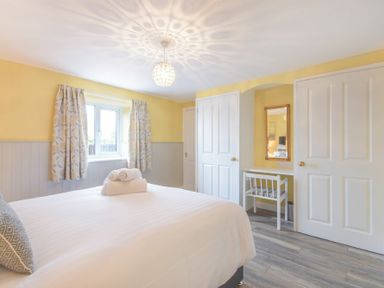 A bedroom with a bed towels on it curtains on window a white chair and table with mirror on wall at Dairymaids Cottage in Amble