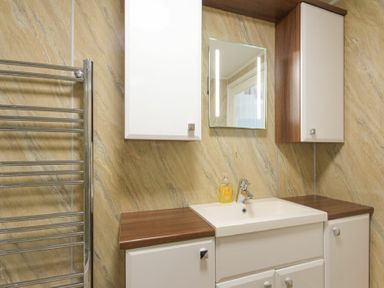 A bathroom sink with cabinets and a mirror above it at Dairymaid's Cottage in Amble