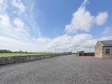 A gravel driveway with a stone wall and a stone building at Dairymaid's Cottage in Amble