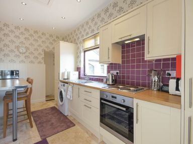 A kitchen with cream cabinets purple tiled backsplash and wooden countertops at Dairyman's Cottage in Amble