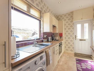 A kitchen with white cabinets a stainless steel sink a washing machine and a white door at Dairyman's Cottage in Amble