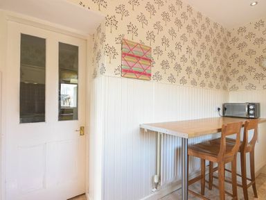 A kitchen corner with a wooden table two wooden chairs a microwave and patterned wallpaper at Dairyman's Cottage in Amble