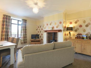 A living room with a sofa dining table chairs television fireplace and wooden sideboard at Dairyman's Cottage in Amble