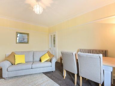 A living room with a grey sofa and yellow cushions next to a dining table with chairs at Dairyman's Cottage in Amble