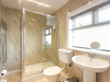 A bathroom with a toilet sink shower glass door and window blinds at Dairyman's Cottage in Amble