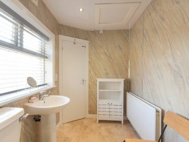 A bathroom with a sink toilet white cabinet radiator and wooden chair at Dairyman's Cottage in Amble