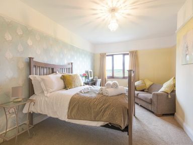 A bedroom with a double bed and rolled towels a sofa next to a window at Dairyman's Cottage in Amble