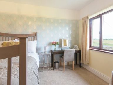 A bedroom with a bed a side table a desk with a mirror and chair near a window at Dairyman's Cottage in Amble