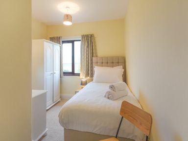 A small bedroom with a single bed a wooden chair a white wardrobe and a window at Dairyman's Cottage in Amble