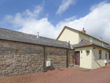 Exterior view of a stone and stucco building with a gravel ground area at Dairyman's Cottage in Amble