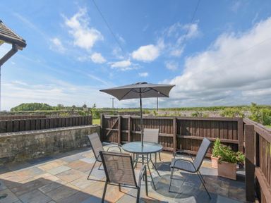 A patio with a glass table umbrella and four chairs surrounded by wooden fences at Dairyman's Cottage in Amble