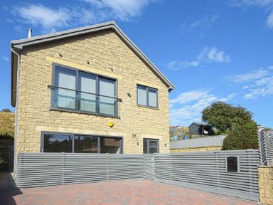 A stone house with gray framed windows and a gray wooden fence around a paved driveway at Riverview (Alnmouth) in Alnmouth