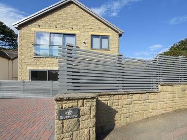 A stone house with large windows and a gray wooden fence at Riverview in Alnmouth
