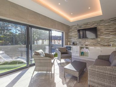 A sitting area with rattan chairs and a table next to sliding glass doors and a wall-mounted TV at Riverview Alnmouth in Alnmouth