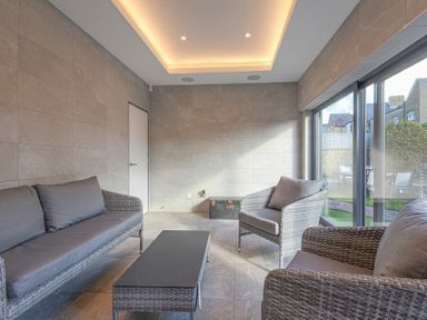 A sitting area with gray cushioned wicker furniture and a black coffee table by large windows at Riverview Alnmouth
