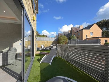 An outdoor patio area with lounge chairs and table with chairs next to a building with sliding glass doors at Riverview Alnmouth in Alnmouth
