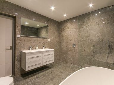 A bathroom with a double sink vanity a large mirror a glass shower enclosure and a white bathtub at Riverview Alnmouth