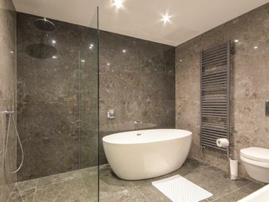A bathroom with a freestanding bathtub a glass shower partition a wall-mounted toilet and a heated towel rail at Riverview Alnmouth