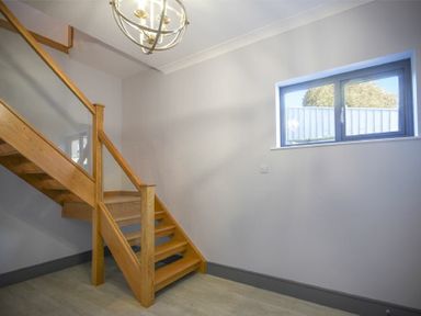 A wooden staircase with glass panels under a ceiling light next to a window in a hallway at Riverview Alnmouth