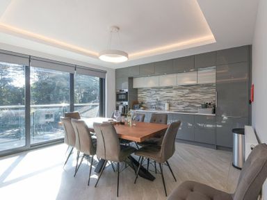 A dining area with a wooden table and six chairs next to a kitchen with grey cabinets and a tiled backsplash at Riverview Alnmouth in Alnmouth
