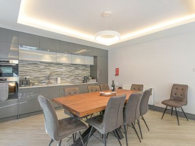 A dining area with a wooden table and grey chairs next to a kitchen with grey cabinets and patterned backsplash at Riverview Alnmouth in Alnmouth
