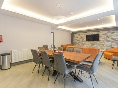 A dining area with a wooden table and gray chairs next to a living room with orange sofas and a television on a textured wall at Riverview in Alnmouth