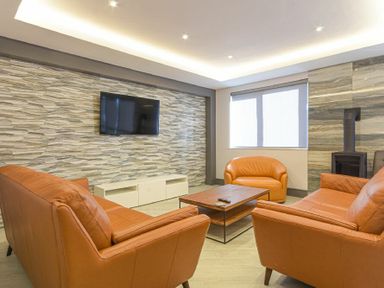 A living room with orange sofas a coffee table a wall mounted TV and a window at Riverview Alnmouth