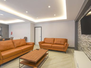 A living room with two brown leather sofas a wooden coffee table a wall-mounted TV and a textured accent wall at Riverview (Alnmouth) in Alnmouth