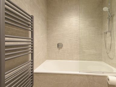 A bathroom with a bathtub shower combination heated towel rail and toilet paper holder at Riverview Alnmouth