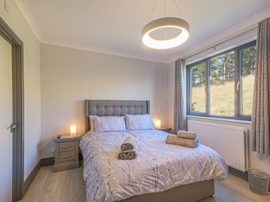 A bedroom with a bed two bedside tables with lamps a window with curtains and folded towels on the bed at Riverview Alnmouth