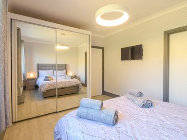 A bedroom with a bed holding folded towels a mirrored wardrobe a wall-mounted TV and two doors at Riverview Alnmouth