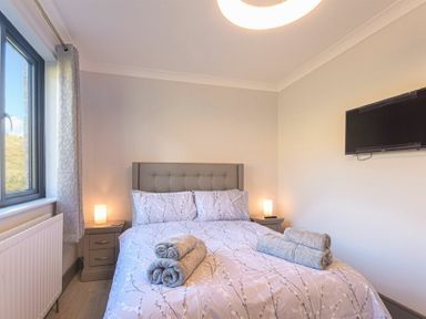 A bedroom with a bed a headboard bedside tables with lamps and a wall-mounted television at Riverview Alnmouth