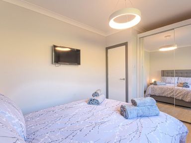 A bedroom with a bed folded towels on it a wall-mounted tv a door and mirrored closet doors at Riverview (Alnmouth) in Alnmouth