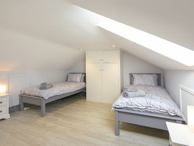 A bedroom with two single beds a cupboard and bedside tables at Riverview Alnmouth